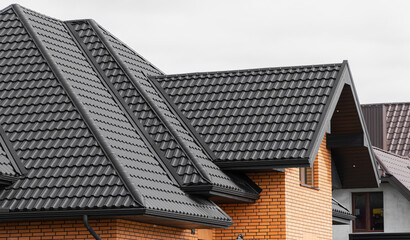 A new house made of yellow bricks and a beautiful black roof. Black corrugated metal profile roof installed on a modern house - obrazy, fototapety, plakaty