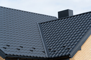 The roof of the house is covered with new black metal tiles. Modern roof made of metal. Modern...