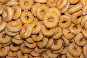 Many sweet and tasty round doughnuts, ring donuts covered with sugar. Chocolate-frosted doughnut. Symbol of sweeties, fried dough. A lot of sweet unhealthy food. Food waste, food production.
