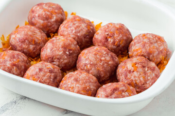 Homemade meatballs with tomato sauce, carrot and spices. Raw ground beef meatballs with rice in a white dish for baking. White marble background. Original way to cook meat