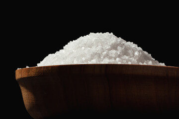 Coarse white salt in a wooden bowl on the black background