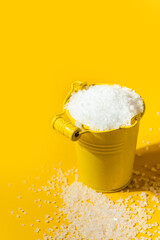 Coarse white salt in a yellow metal small bucket on the yellow background. Free space for text