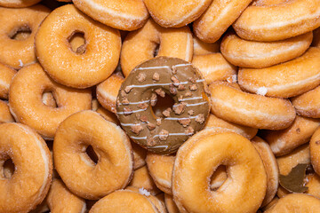 Many sweet and tasty round doughnuts, ring donuts covered with sugar. Chocolate-frosted doughnut. Symbol of sweeties, fried dough. A lot of sweet unhealthy food. Food waste, food production.