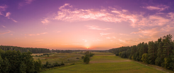 Rural landscape in the evening with the beautiful burning sky. Aerial view. Panoramic view of pine forest, and fields during sunset. Horizontal banner