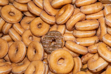 Many sweet and tasty round doughnuts, ring donuts covered with sugar. Chocolate-frosted doughnut. Symbol of sweeties, fried dough. A lot of sweet unhealthy food. Food waste, food production.
