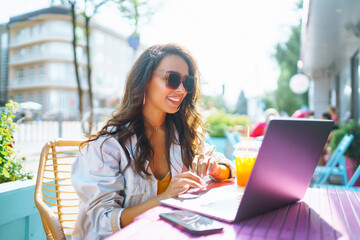 Young and cheerful woman on the terrace chatting on Skype, talking on a webcam, having a video...