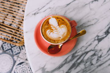 Pink cup of cappuccino with latte art on marble table