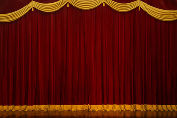 Theatrical stage curtain red heavy velvet adorned with gold fringe at the bottom and top.