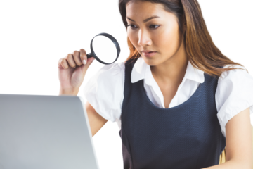 Businesswoman looking through magnifying glass and using laptop