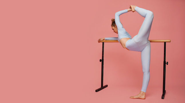 Female ballet dancer blonde hair stretching her leg. Side view of young woman preparing for a ballet class in studio. in pink background