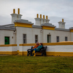 Romantic couple sitting on a bench beneath a lighthouse on the coast in Scotland 