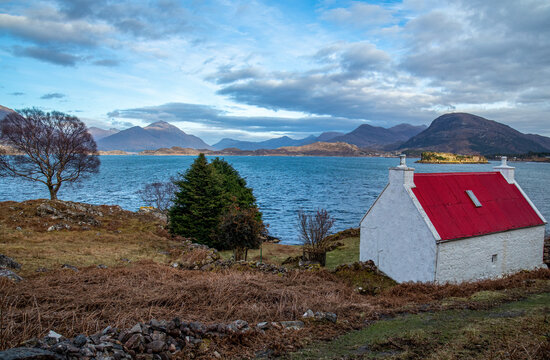 red roofed cottage painted white with a view over a scottish lake and the mountains