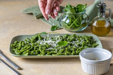 Spinach spatzle are the typical Tyrolean green dumplings or gnocchi on green plate with grated cheese and olive oil. Woman's hand is pouring cheese to the dish