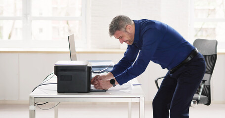 Irritated Businessman Looking At Paper Stuck In Printer
