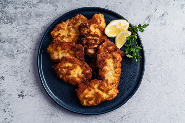 Schnitzel with slice of lemon on black plate on grey background