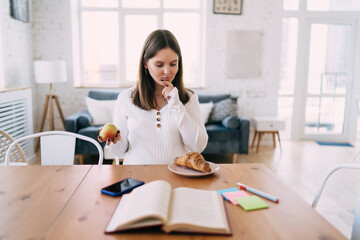Young expectant woman sitting at table choosing snack in kitchen