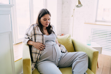 Happy pregnant woman sitting in armchair at home