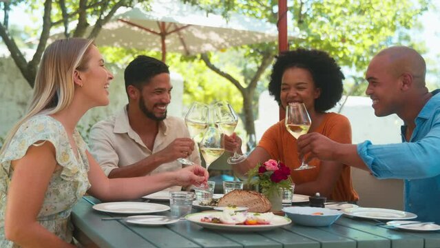 Group of friends visiting vineyard sitting at outdoor table of restaurant and making a toast with white wine - shot in slow motion