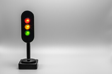 Miniature traffic light with red, orange and green light on. Studio shot. Silver grey empty...