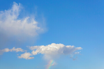 Fototapeta na wymiar Light blue sky and smooth white clouds. Rainbow. Copy space