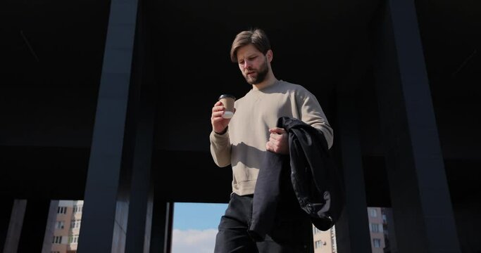 Close up of a man drinking take away coffee. Young man walks around modern urban area, with take away coffee.