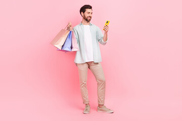 Full length photo of positive cute guy dressed teal shirt holding bargains texting apple samsung gadget isolated pink color background