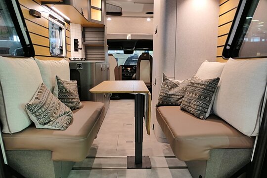 Side seats with pillows and portable dining table in modern german camper van Hymer Venture S 4x4, wooden padding on walls visible. Displayed on Caravan bike travel expo in Nitra, Slovakia, march 2023