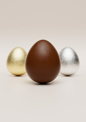 Milk chocolate easter eggs with gold and silver Aluminium foil on pale background.	
