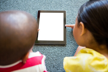 Siblings using digital tablet on carpet