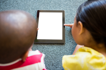 Siblings using digital tablet on carpet