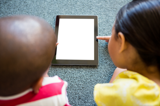 Siblings using digital tablet on carpet