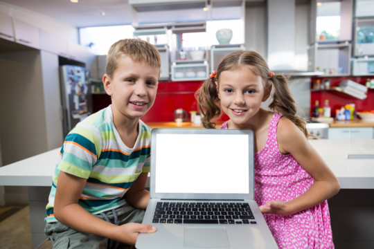 Smiling siblings holding laptop in kitchen