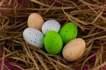 Multi-colored eggs lie in the straw. Easter nest with eggs painted in different colors. On a pink background, a nest with beautiful Easter eggs. Easter holiday concept.