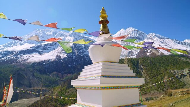 Parallax of Stupa with prayer flags waving in the wind and picturesque sunny Himalaya mountain peak views in the distance, Annapurna, Nepal