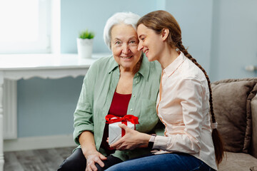 A smiling caring daughter presents a gift to her elderly mother on Women's Day.