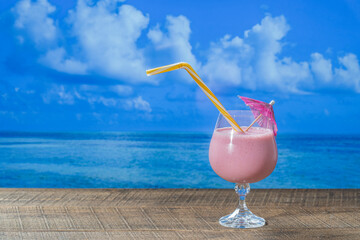 Healthy cold strawberry smoothie in a glass wineglass on wooden table with the sea water background on a sunny summer day, closeup, copy space