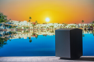 Black acoustic sound speaker on a wooden table against the tropical beach background with sea water...