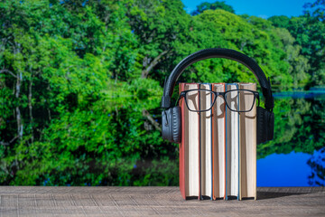 Set of books, headphones and eyeglasses on wooden table with the lake water and forest background...
