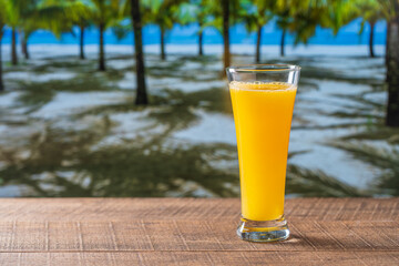 Freshly squeezed orange juice in glass on wooden table near sea on sunny summer day in tropical beach cafe, close up, copy space. Glass of fresh fruit orange juice