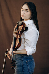 A beautiful girl holds a violin in her hands. Violinist in white shirt and jeans