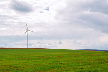 Fototapeta na wymiar Beautiful wide shot of a single white wind turbine standing on a green meadow.