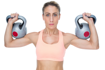 Serious female crossfitter lifting kettlebells looking at camera