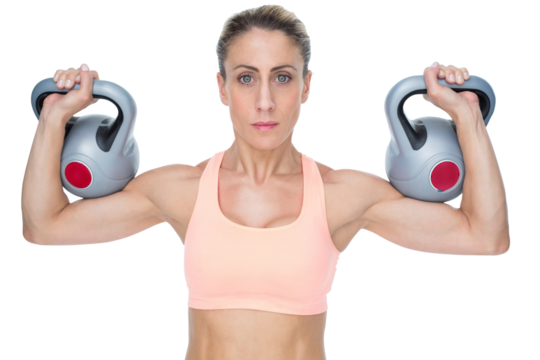Serious female crossfitter lifting kettlebells looking at camera