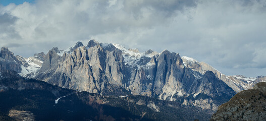 Ośnieżone szczyty gór, panorama, początek wiosny, u podnóża już zieleń. Pastelowe chmury nad szczytami. Słońce miejscami oświetla zbocza. Plamy słońca. © Tomasz