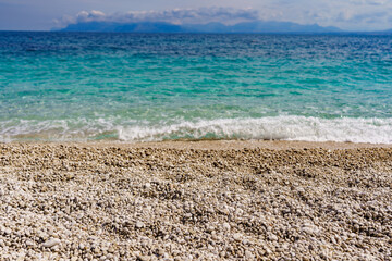 A beautiful beach where instead of sand there are small round pebbles overlooking the turquoise sea.