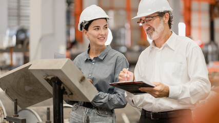 Two professional engineer,worker,technician use clipboard discuss work, walk in steel metal manufacture factory plant industry. Black African American man and woman wear hard hat check quality machine