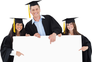 Three graduates pointing to the blank sign as they look at the camera