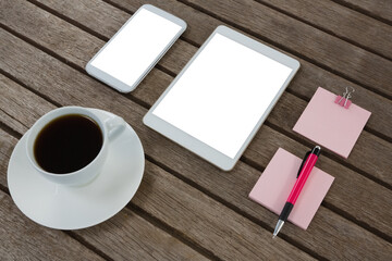 Black coffee, mobile phone, digital tablet, pen and sticky note on wooden plank
