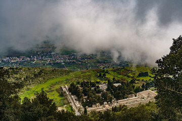 A beautiful view from above, just below the cloud line, on a hillside covered with dense foliage and the town below.