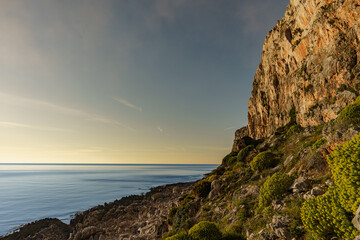 A beautiful sunset over the warm sea to which rocky mountain peaks and walls descend.